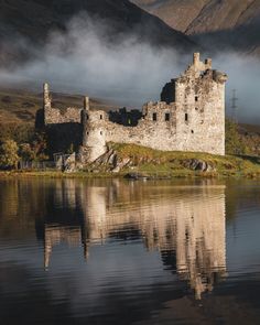 an old castle sitting on top of a hill next to a body of water with mountains in the background