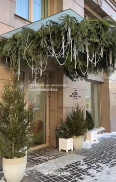 a building with christmas decorations hanging from it's front door and two potted trees on the sidewalk