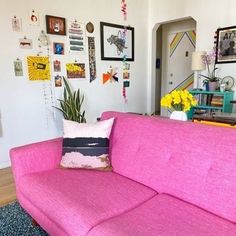 a pink couch in a living room with pictures on the wall behind it and a potted plant