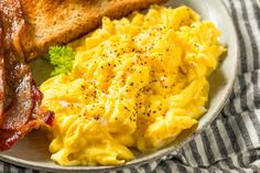 a white plate topped with eggs and bacon next to toast on a striped table cloth