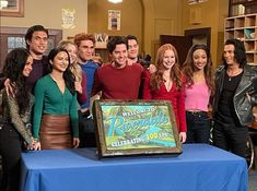 a group of people standing around a table with a sign on it that says welcome to riverdale celebrating 100 years