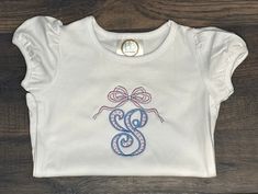 Girls Classic Bow Monogram Shirt. Embroidered Girls Monogram Outfit. Classic Bow Monogram Shirt. Toddler Girl Classic Bow Monogram Outfit. This design comes on a 100% cotton shirt, bubble, or Bodysuit! Each item is made to order specifically for you! Please select your choice of style. Please put Letter to be monogrammed in the personalization if applicable. Due to personalization I do not accept returns, however, if you are unhappy with your purchase in any way please reach out to me. Check out some of my other designs! https://stablestitchesshop.etsy.com THANK YOU so much for shopping small Cute White Top With Machine Embroidery, Cute White Tops With Machine Embroidery, Spring Tops With Custom Embroidery, Cotton Tops With Embroidered Graphics As Gift, Cute Fitted Tops With Custom Embroidery, Cute Fitted Top With Custom Embroidery, White Monogrammed Short Sleeve Top, White Monogram Short Sleeve Top, Short Sleeve Cotton Monogram Top