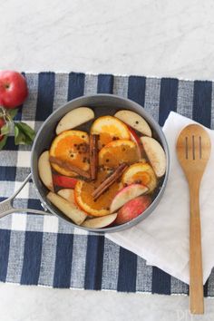 apples and cinnamon sticks are in a pan on a tablecloth with a wooden spoon