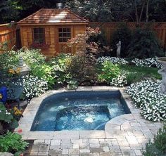 an outdoor hot tub in the middle of a garden with flowers and trees around it