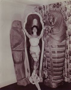 an old black and white photo of a woman standing next to two egyptian statues