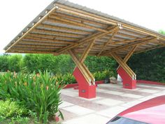 a red car is parked under a wooden structure in front of some bushes and trees