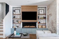 a living room with a fireplace and television on the wall, surrounded by bookshelves