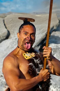 a man with no shirt on holding a stick and wearing an animal skin suit while standing in the snow