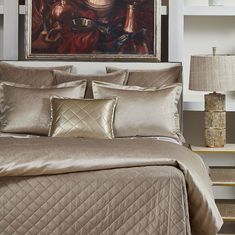 a bed with gold comforter and pillows in a bedroom next to a painting on the wall