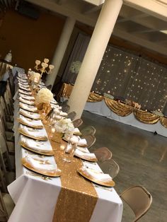 a long table is set up with gold and white plates, silverware, and napkins