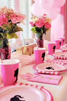 the table is set with pink and black plates, cups, and vases filled with flowers