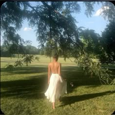 a woman in a white dress is walking through the grass with her back to the camera