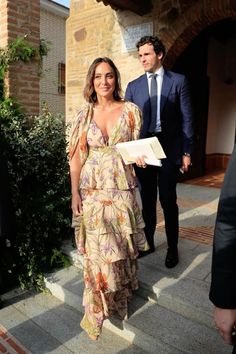 a woman in a long dress is walking down the street with a man behind her