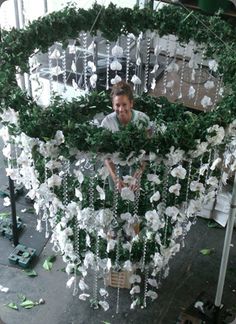 a woman standing in front of a green and white sculpture with flowers hanging from it's sides