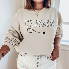 "The \"Nurse Sweatshirt\" is a sturdy and warm sweatshirt bound to keep you warm in the colder months. Perfect cozy sweater or gift idea! A pre-shrunk, classic fit sweater that's made with air-jet spun yarn for a soft feel and reduced pilling. Sweatshirt details: * 50% cotton, 50% polyester * Pre-shrunk * Classic fit with no center crease * 1x1 athletic rib knit collar with spandex * Air-jet spun yarn with a soft feel and reduced pilling * Double-needle stitched collar, shoulders, armholes, cuffs, and hem * Model is wearing a size L *If you'd like an oversized fit please order 1-2 sizes larger than your normal size. For any sizing recommendations please message us :) Additional styles & custom orders: All of our designs are listed in several different styles (tees, tanks, hoodies, hats) th School Sweatshirts Designs, Basketball Treats, Cricut Clothing, Travel Sweatshirt, School Sweater, Custom Crewneck Sweatshirts, Custom Crewneck, Trendy Tees, Sweatshirt Details