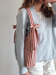 a woman drinking from a cup while wearing a red and white striped bow tie bag