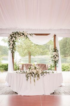 a table with white flowers and greenery is set up for an outdoor wedding reception