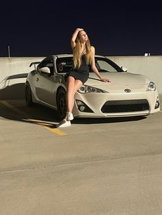 a woman sitting on the hood of a sports car in front of a parking lot