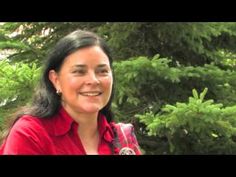 a woman in a red shirt is smiling at the camera and trees behind her are green