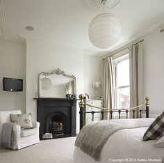 a bedroom with a bed, chair and mirror in it's corner area next to a fireplace