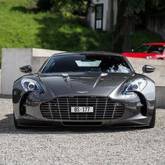 a grey sports car parked in front of a red car on the side of a road