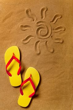 a pair of yellow and red flip flops sitting on top of a sandy beach