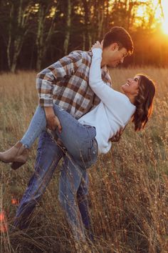 a man holding a woman in the middle of a field with tall grass at sunset