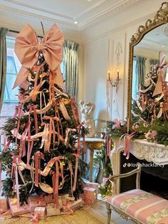 a decorated christmas tree in a living room with pink bows on it's top