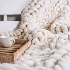 a coffee cup on a wooden crate under a chunky blanket with white yarn in the background