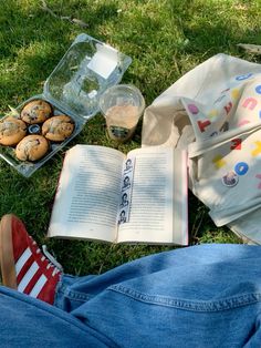 an open book and some muffins are on the grass next to a bag