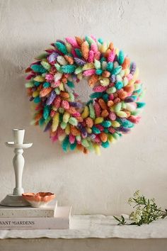 a multicolored wreath hangs on the wall next to a candle holder and books