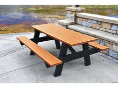 a wooden picnic table sitting on top of a sidewalk next to a stone wall and water