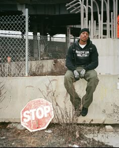 a man sitting on top of a cement wall next to a stop sign