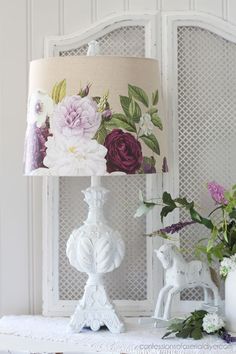 a lamp with flowers on it sitting next to a vase and potted plant in front of a window