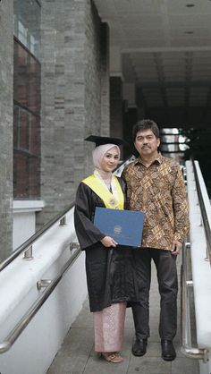 a man and woman in graduation gowns standing next to each other on the stairs