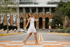 a woman in a white dress is crossing the street and talking on her cell phone