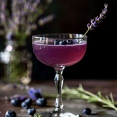 a glass filled with purple liquid next to some blueberries and lavender sprigs