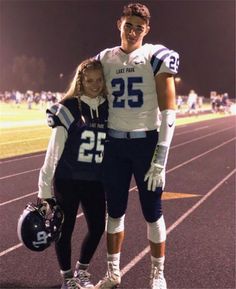 a man and woman posing for a photo on a football field at night with lights in the background