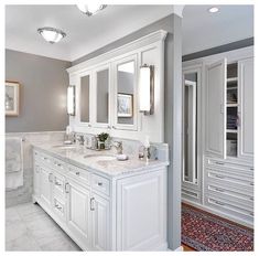 a bathroom with two sinks, mirrors and cabinets in white marble counter tops on either side of the bathtub