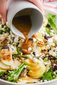 someone pouring dressing onto a salad with apples and cranberries on top in a white bowl