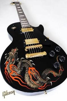 a black guitar with red and yellow dragon decals on it's body, sitting against a white background