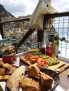 bread, tomatoes and olives sit on a table overlooking the ocean