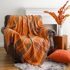 an orange plaid blanket sitting on top of a couch next to a vase with flowers