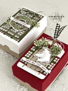 two boxes with christmas cards on them sitting on top of snow covered ground and one has a pair of ice skates