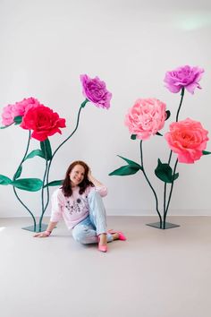 a woman sitting on the ground in front of three paper flowers with leaves and stems