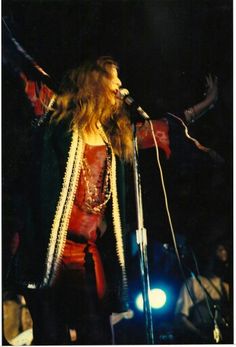 a woman with long hair standing in front of a microphone and holding her arms out