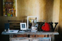 an old table with many items on it and a painting in the corner behind it