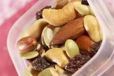 a plastic container filled with nuts and raisins on top of a pink surface