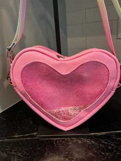 Bonjour!  The Lil' Heartbreaker is a heart shaped bag with amazing details at every curve!  It measures approximately 9" wide, 9" tall, and 3" deep.  It has a double zipper closure at the top of the heart and the strap connectors are on either side of the zipper.  It features a clear vinyl front with iridescent pink glitter inside that moves and jiggles as you walk.  So cute!  The pink vinyl outer is so soft and the silver hardware contrasts it nicely.  The 1" strap connectors are reinforced with heart shaped rivets, the zipper pulls say "Bee mine", and there is a tag on the back that says, "Don't go break-in' my heart".  The strap is removable and adjustable in a rainbow colored seatbelt webbing.  Open it up to reveal hearts and polka dots water resistant canvas lining  and a white mesh s Trendy Heart-shaped Shoulder Bag With Zipper Closure, Valentine's Day Heart-shaped Bag With Removable Pouch, Valentine's Day Heart-shaped Shoulder Bag, Valentine's Day Crossbody Shoulder Bag With Zipper, Heart-shaped Shoulder Bag With Heart Print, Heart-shaped Shoulder Bag With Zipper Closure, Heart-shaped Pink Bag With Removable Pouch, Heart-shaped Bag With Heart Detail For Everyday, Valentine's Day Gift Shoulder Bag With Zipper Closure