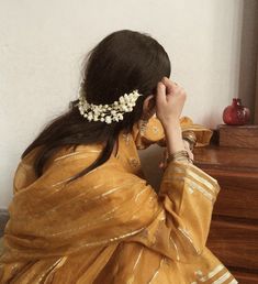 a woman in a yellow sari is sitting on a chair with her hands to her face